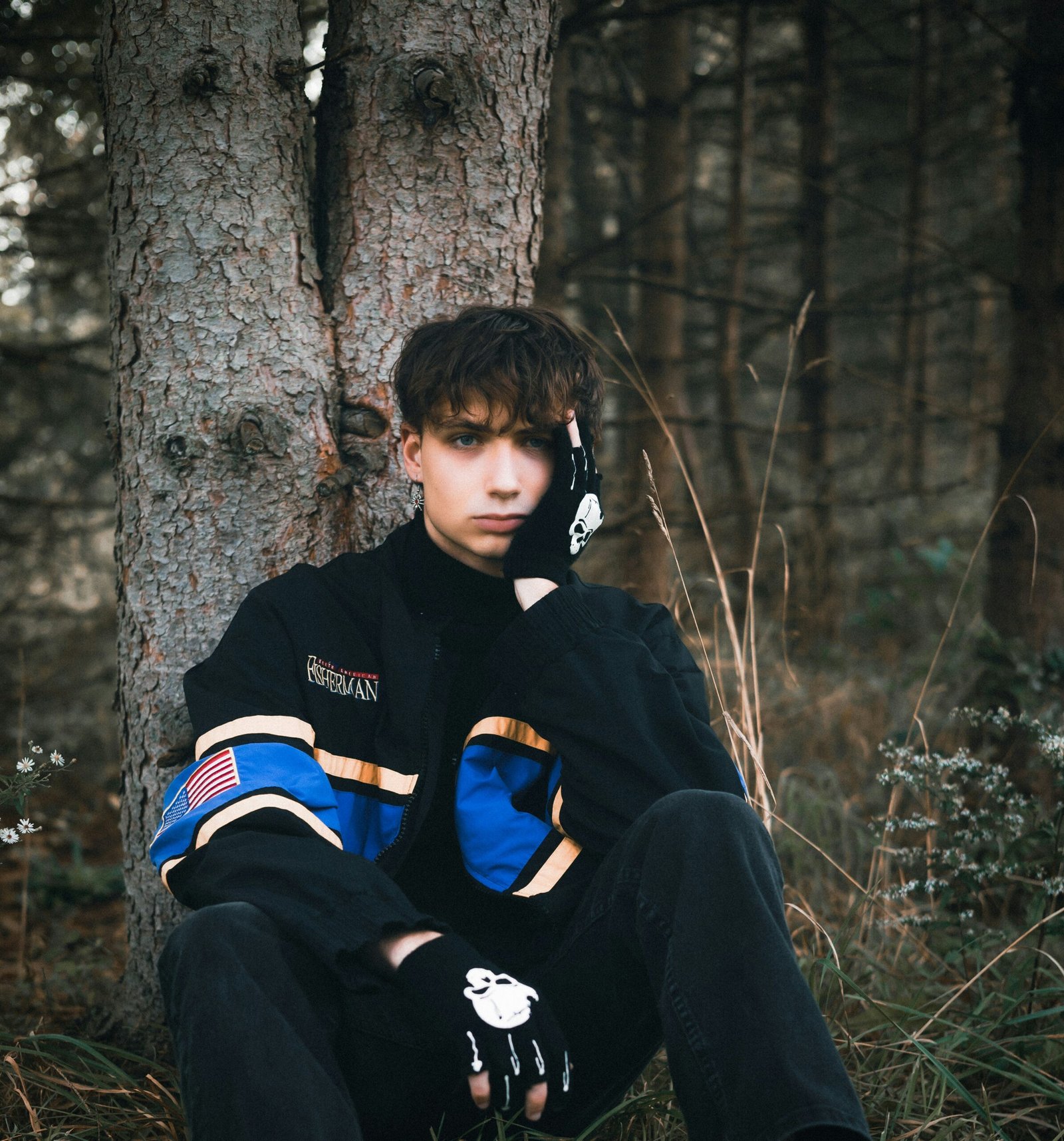 a young man sitting in the grass next to a tree